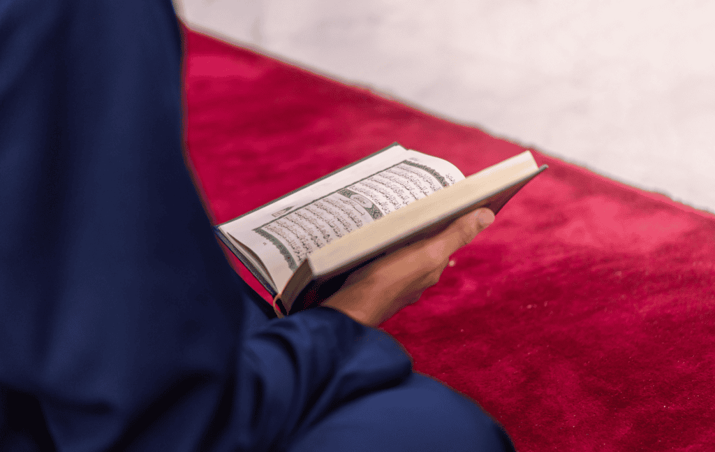 L'Imam, assit sur un tapis rouge, tenant le Coran dans sa main lors d'une sépulture musulmane.
